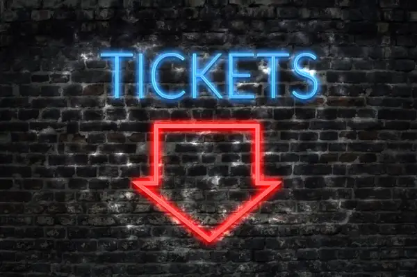 Napis "TICKETS" neonem w kolorze niebieskim i czerwona strzałka w dół na ceglanej ścianie.