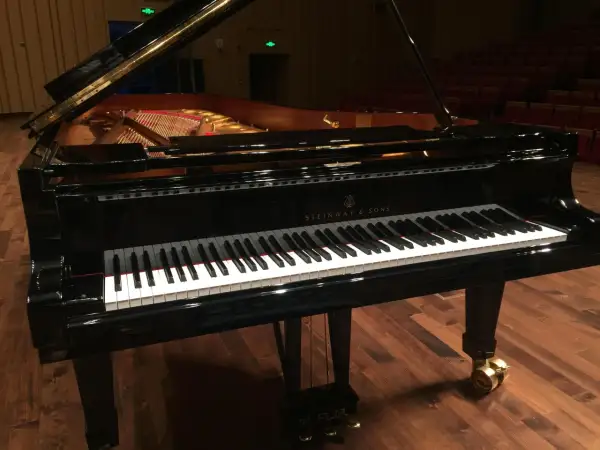 Czarny fortepian Steinway & Sons z otwartą klapą, na drewnianej scenie.
