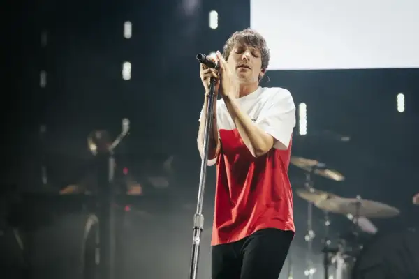 Louis Tomlinson śpiewa na koncercie w Polsce, w czerwono-białej koszulce, z zamkniętymi oczami.