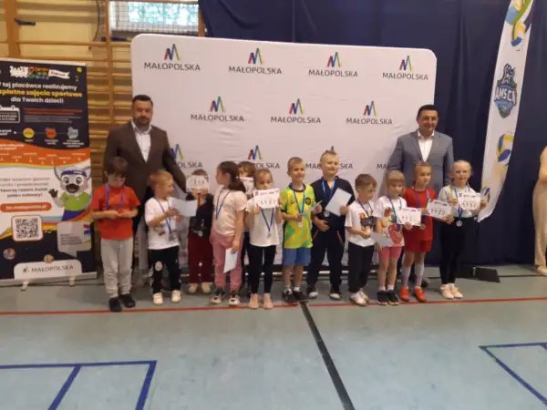 Dzieci z dyplomami i medalami stoją przed banerem "Małopolska".