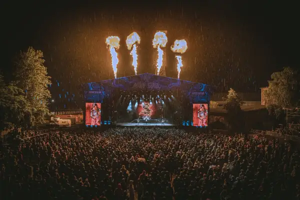 Koncert na Mystic Festival w deszczu, z płomieniami nad sceną i tłumem fanów.