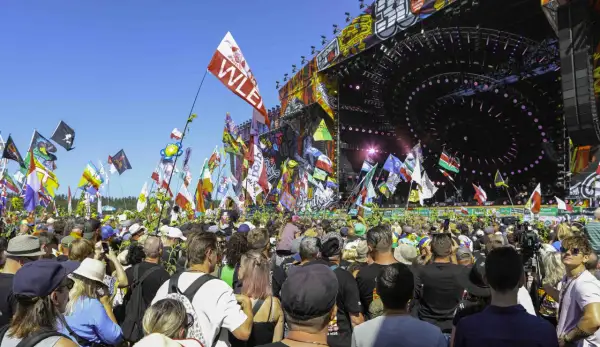Tłum ludzi na festiwalu muzycznym z flagami i sceną w tle.