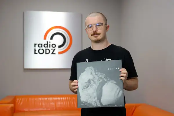 Mężczyzna w okularach trzyma płytę winylową The Cure "Songs of a Lost World" na tle logo Radia Łódź.