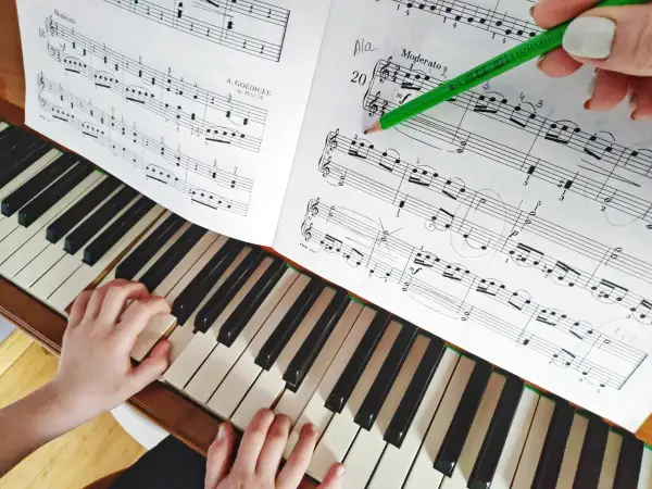 Dziecko uczy się gry na keyboardzie, ćwicząc nuty z podręcznika. Zielony ołówek zaznacza fragment do nauki.