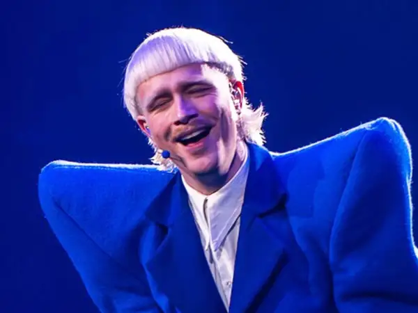 Joost Klein w niebieskiej marynarce, śpiewający na scenie z zamkniętymi oczami.