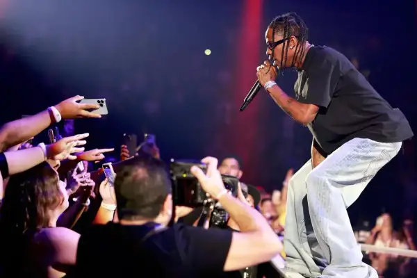 Travis Scott koncert: artysta śpiewa do mikrofonu, a fani z telefonami w dłoniach nagrywają występ.