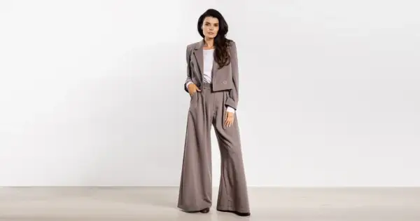 Kobieta w eleganckim, szarym garniturze z szerokimi spodniami i krótką marynarką.