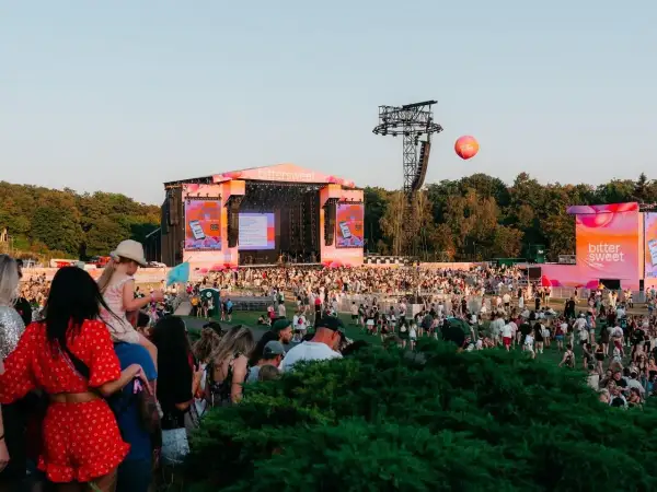 Tłum ludzi na festiwalu Bittersweet, scena w tle, różowe dekoracje i balon unoszący się na niebie.