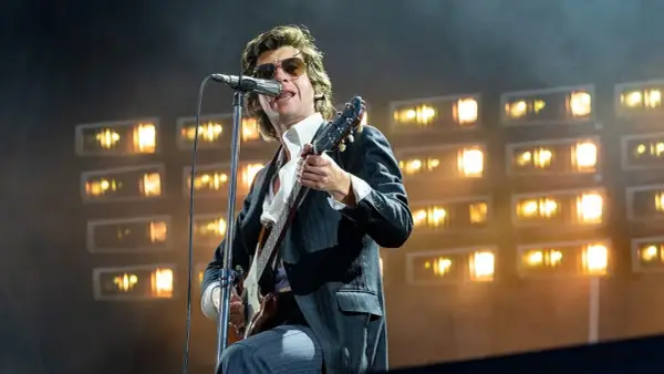 Alex Turner z Arctic Monkeys na scenie, w okularach i garniturze, gra na gitarze podczas jednego z niezapomnianych koncertów.