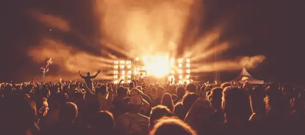 Tłum ludzi na festiwalu muzycznym, scena z jasnymi światłami i dymem.