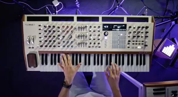 Dłonie grające na białym syntezatorze Arturia PolyBrute 12 z drewnianymi elementami.