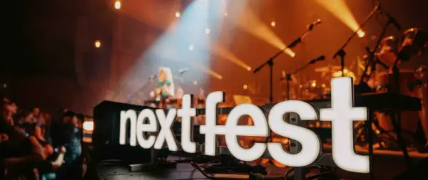 Światła sceny oświetlają napis "next fest" i artystkę grającą na gitarze.