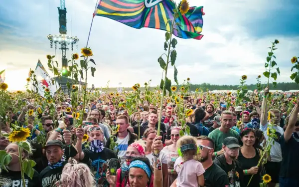 Tłum ludzi na festiwalu Pol'and'Rock trzymający słoneczniki i flagi, z widoczną sceną w tle.