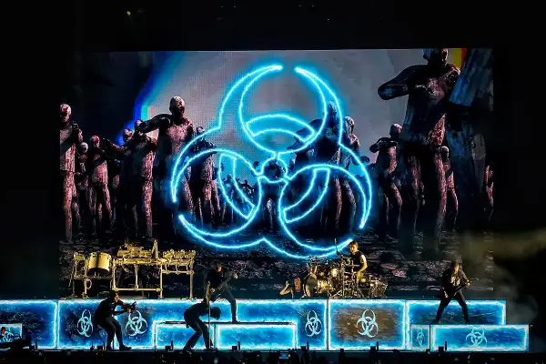 Koncertowy zespół na tle ekranu z symbolem biohazard i zombie.