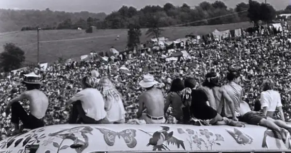 Widok z góry na tłum ludzi na festiwalu Woodstock '69, z kilkoma osobami siedzącymi na ozdobionej ciężarówce.