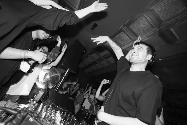 Energiczny DJ Fred Again w Polsce, tłum szaleje przy muzyce, dyskotekowa kula błyszczy.