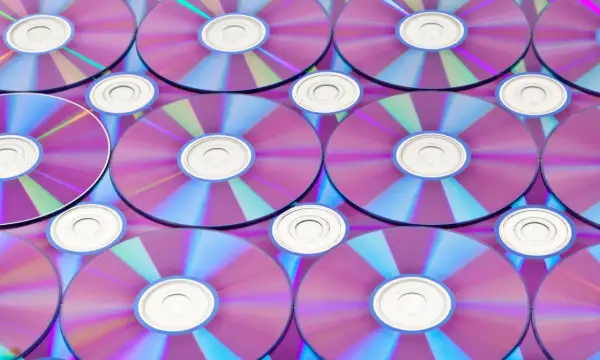 Stos płyt CD/DVD z fioletowo-niebieskimi refleksami, widoczne środkowe otwory.