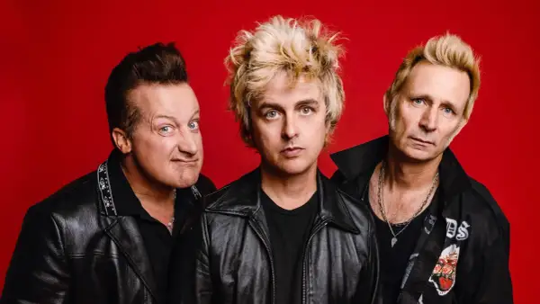 Trzech członków zespołu Green Day na czerwonym tle, w skórzanych kurtkach.