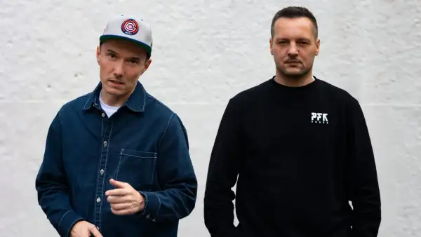 Dwóch członków Paktofoniki, jeden w czapce z daszkiem i granatowej kurtce, drugi w czarnej bluzie z logo PFK.