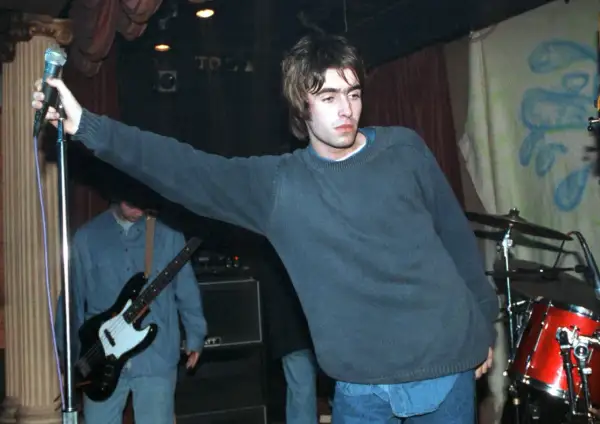 Liam Gallagher z Oasis śpiewa na scenie, w tle basista i perkusja. To klasyczne oasis utwory.